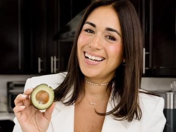 Woman smiling while holding half an avocado.