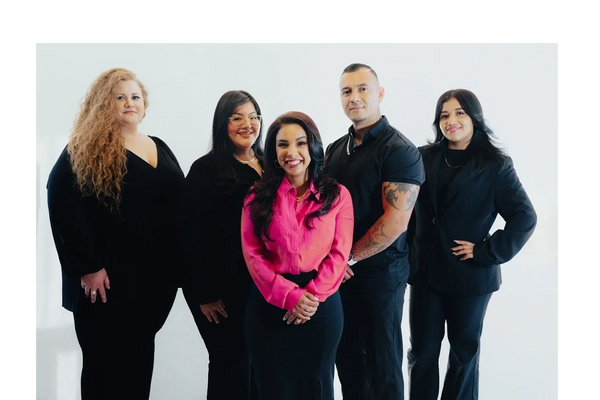 Five professionals posing confidently, one wearing a vibrant pink shirt, others in black attire.