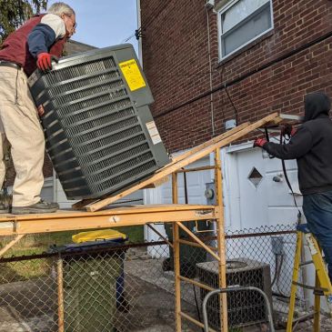 Two men moving an HVAC unit up a ramp into a building.