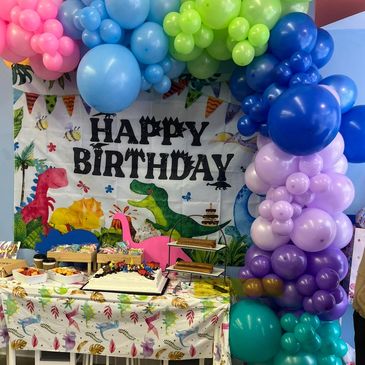 Colorful dinosaur-themed birthday party with balloons and cake.