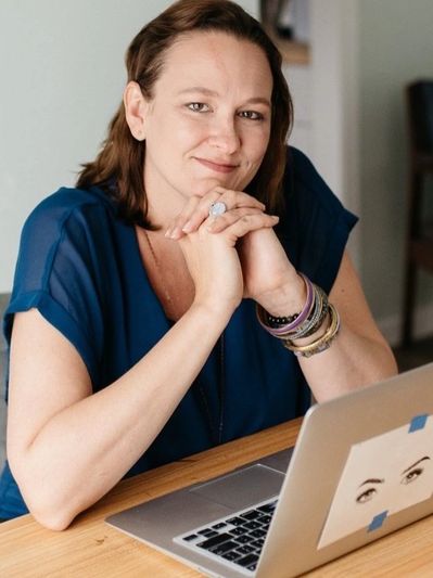 Woman in blue top sitting at a table with a laptop.
