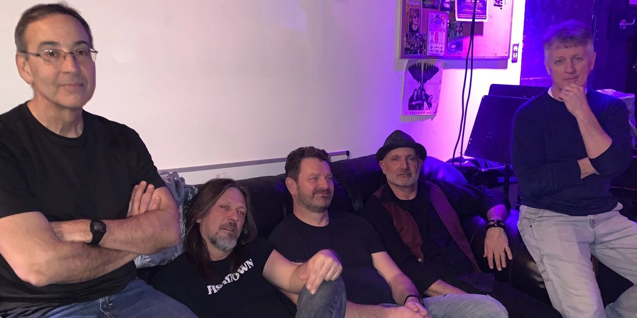 Five men casually seated together on a couch in a relaxed setting.