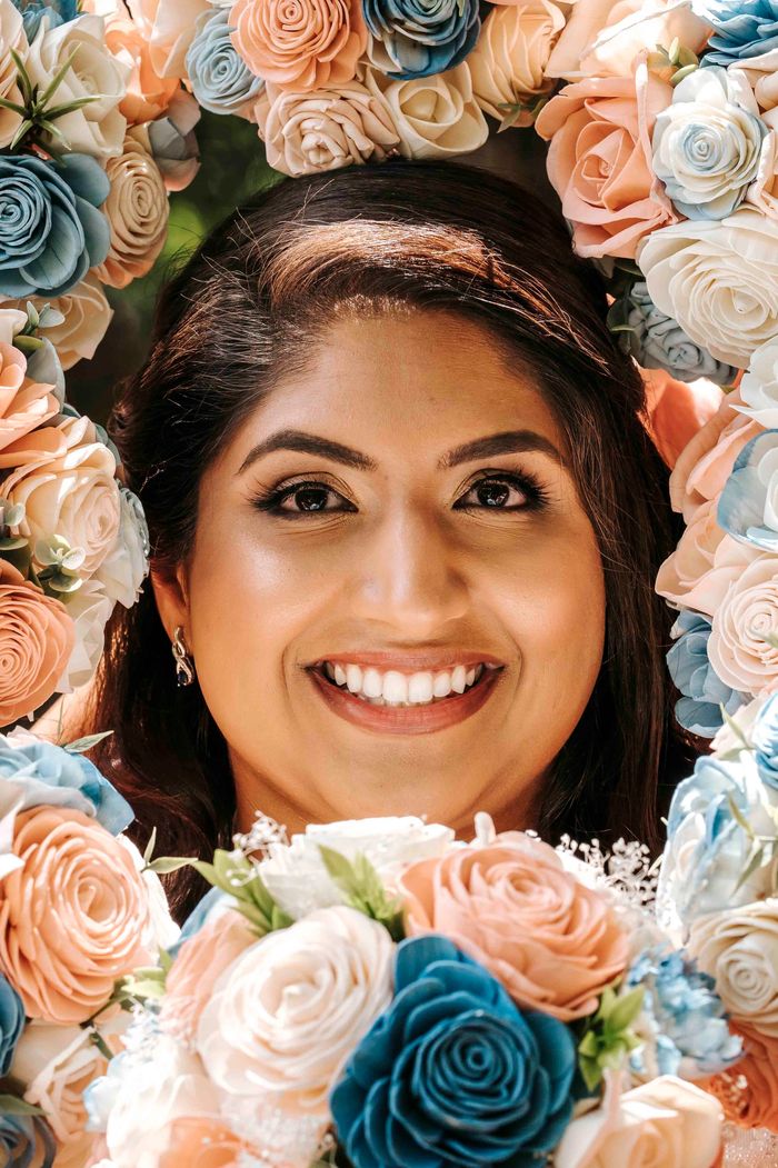 Smiling bride surrounded by flower bouquets in shades of pink, white and blue.
