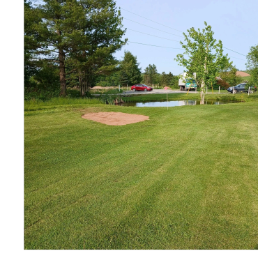 Golf course with pond and parked cars nearby.