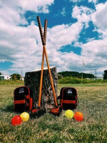 Polo mallets, balls, and gear on grass against blue sky.