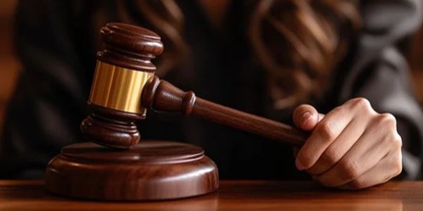 Judge's hand holding a wooden gavel on a desk.