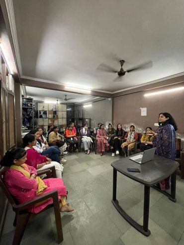 A group of women seated in a room attentively listening to a presenter with a laptop.