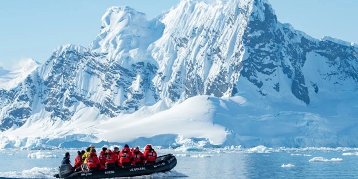 Tourists in a boat exploring icy Antarctic waters near towering snow-covered mountains.