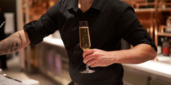 Virgin Voyages Bar Tender with tattoos in a black shirt serving Champagne at the Sip Lounge