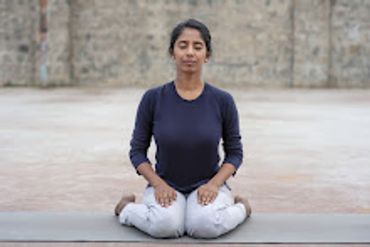 A woman meditating outdoors in a seated posture.