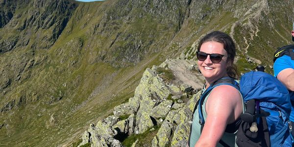 Lara smiling in the sunshine in her happy place - on the top of a mountain in the Lake District.