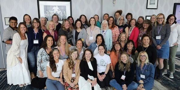 A large group of smiling women gathered indoors for a group photo.