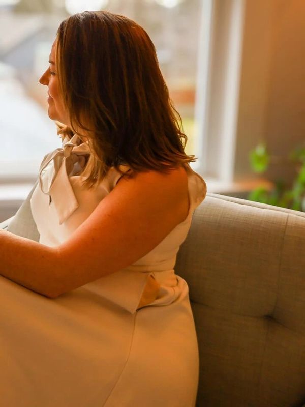Woman in a white dress sitting on a couch in warm lighting.