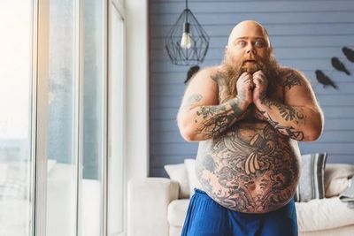 Large man with many tattoos holding his chin wondering if his laser tattoo removal will be painful