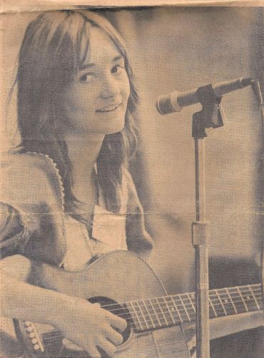 Young woman playing guitar and singing into a microphone.