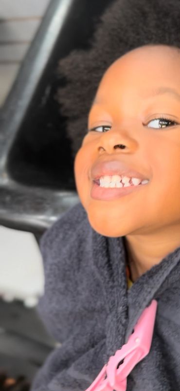 Smiling child with natural hair wrapped in a towel at a salon.