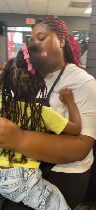 A woman with red braids hugs a child with braided hair in a cozy embrace.