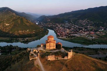 Ancient fortress on a hill overlooking a river and town surrounded by mountains.