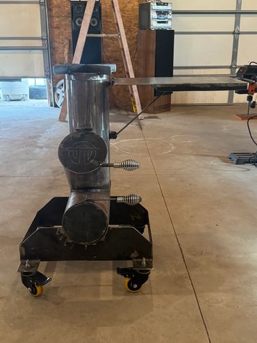 Custom metal stove on wheels with a flat cooking surface in a garage.