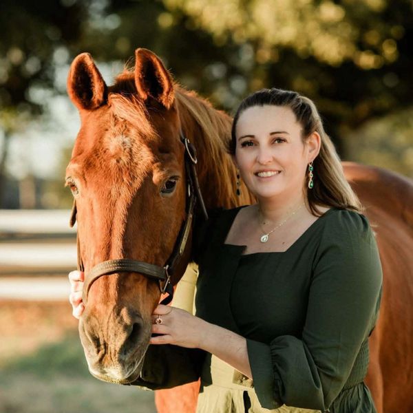 A woman happily posing with a brown horse outdoors.