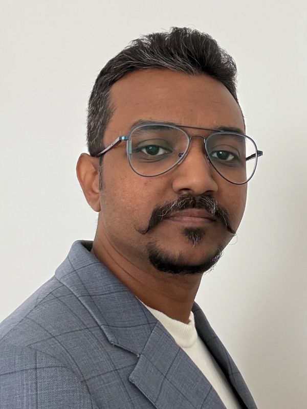Man with glasses and a stylish mustache wearing a gray suit jacket.