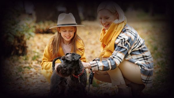 Woman and girl petting a black dog outdoors.