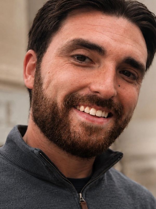 Smiling bearded man in a gray zip-up sweater.