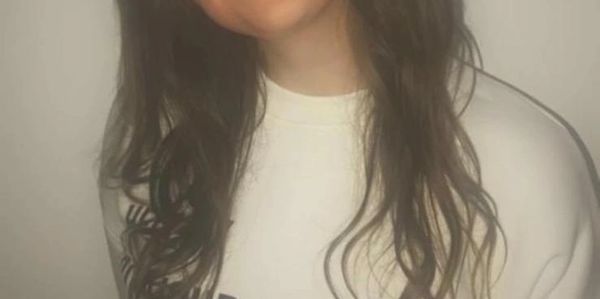 Young woman smiling in a white sweatshirt.