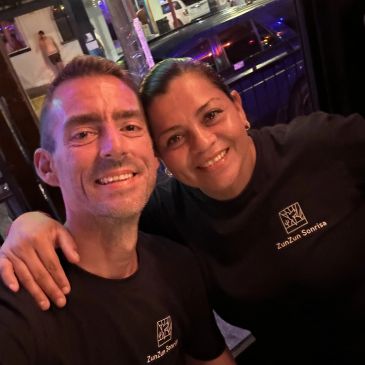 Smiling couple wearing matching black shirts, posing for a selfie in a cozy setting.