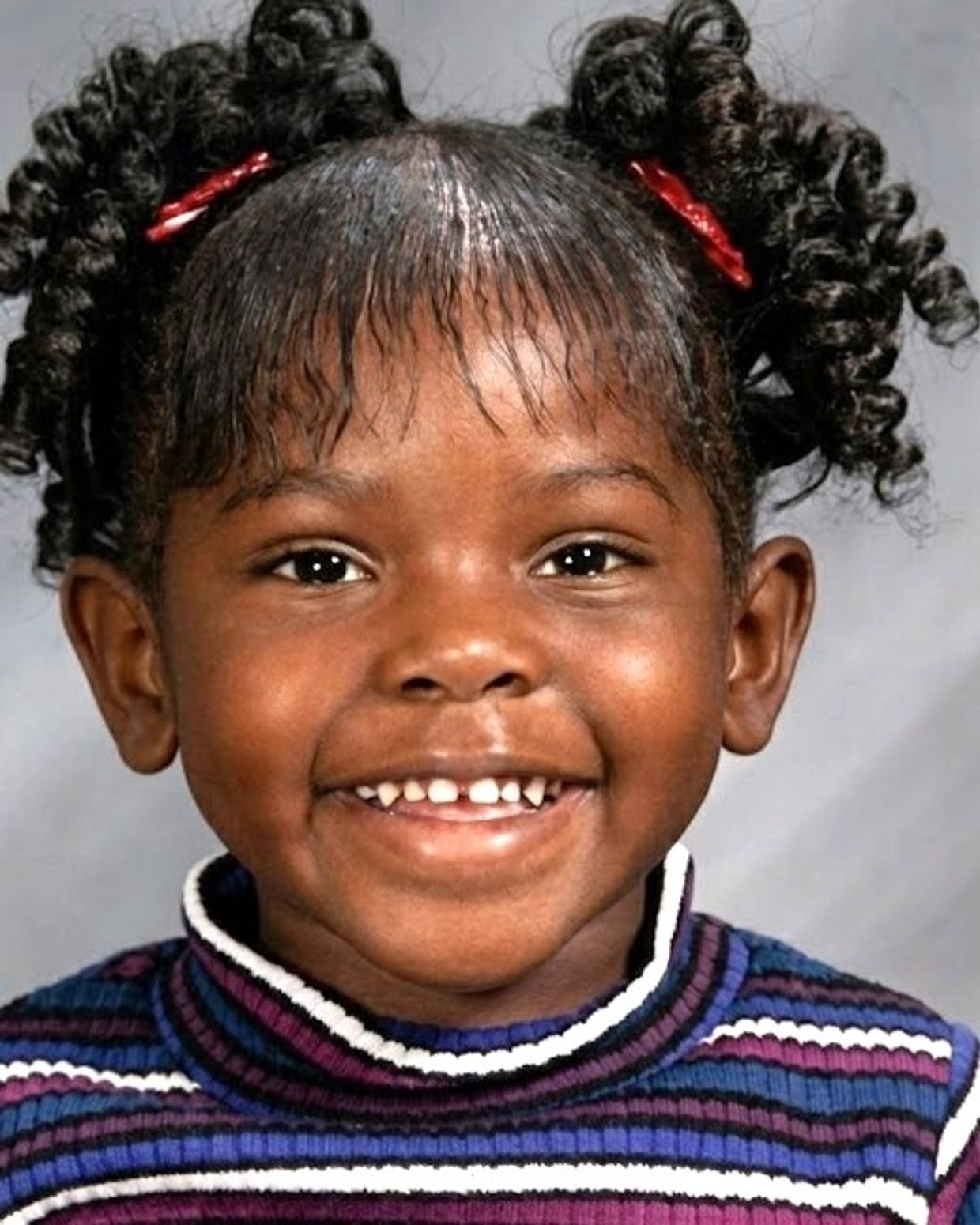 Smiling young girl with curly hair and colorful striped sweater.