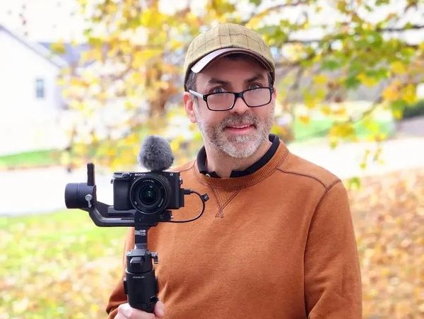 Man holding camera with microphone outdoors.