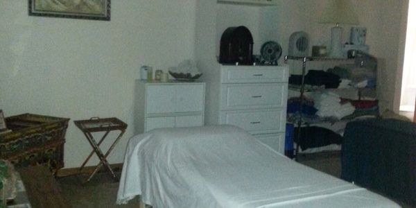 Clean artistic Massage room, two massage tables, white cabinets, chrome wire shelves with linens.