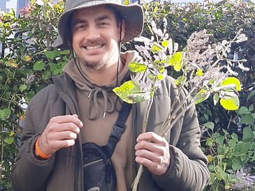 Man in outdoor gear smiling and holding plant branches.