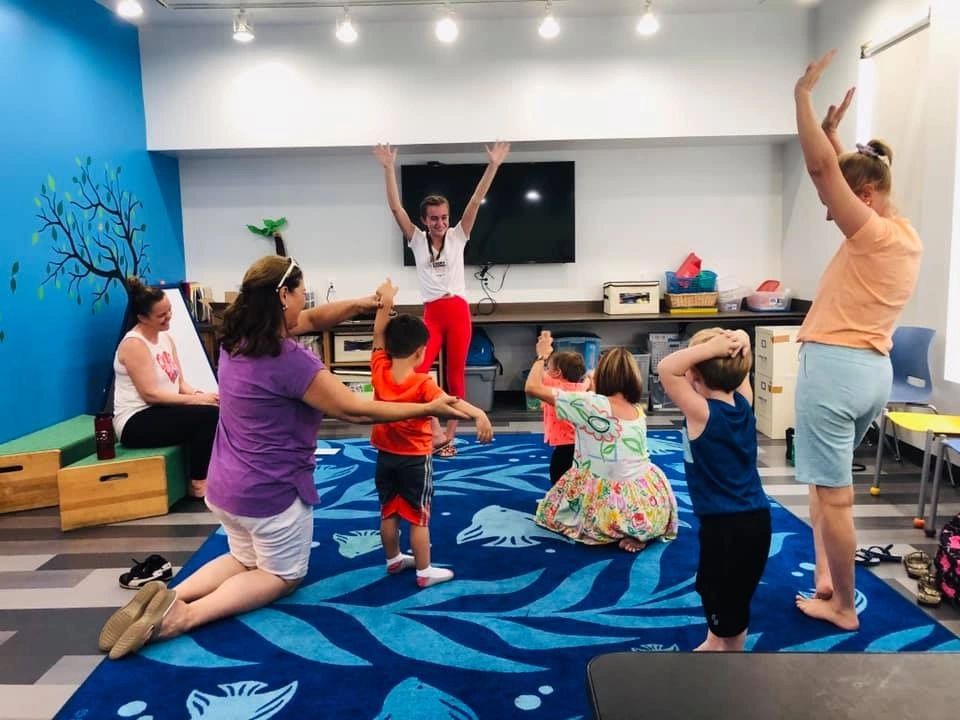 Girl yoga instructor teaching yoga tree pose to group of parents and kids