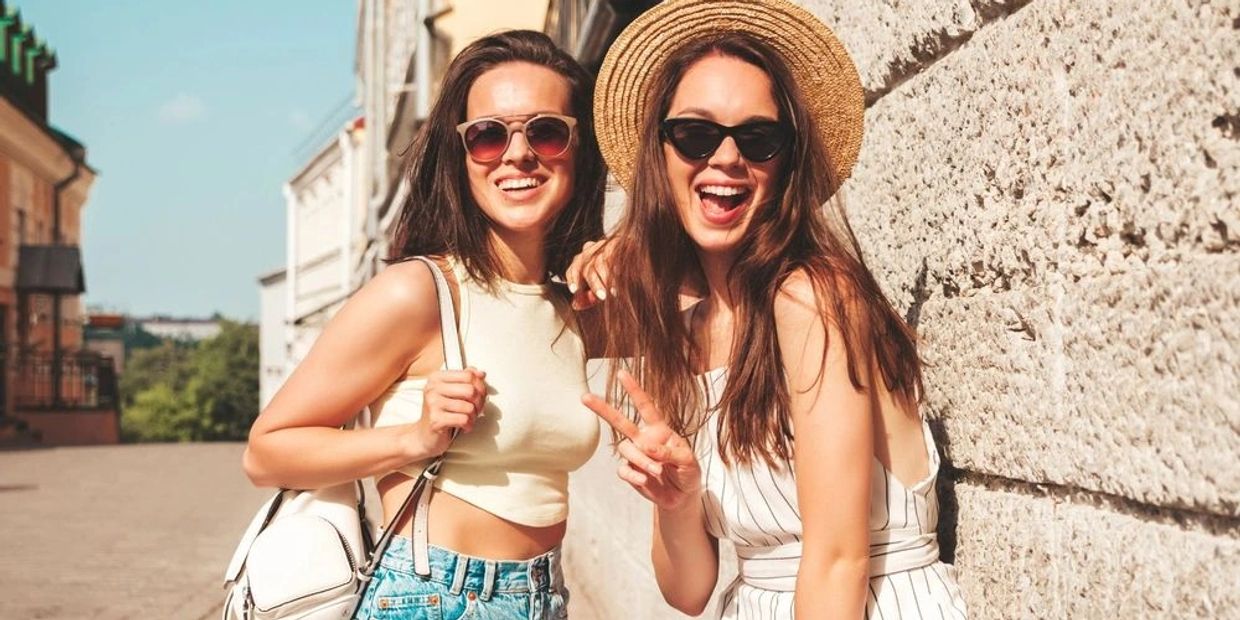 Zwei junge Frauen lachen und posieren draußen.