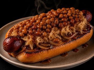 A hot dog topped with baked beans and sauce.