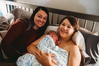 doula and client in bed with new baby on chest covered with blanket after home birth 
