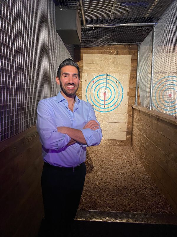Man smiling confidently in an axe-throwing lane with a target behind him.
