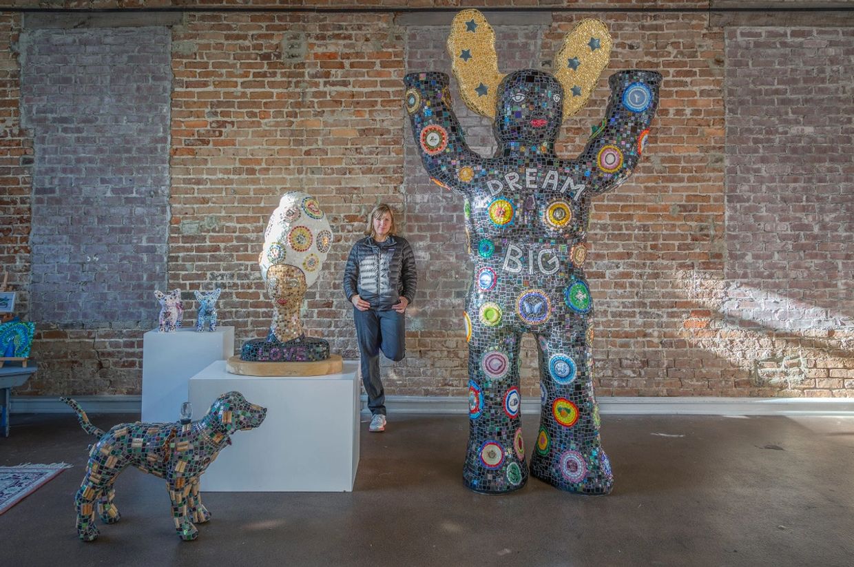 Person standing among colorful mosaic sculptures in a gallery.
