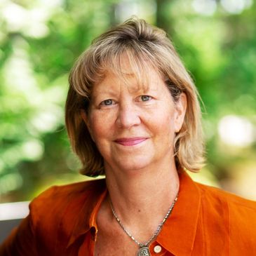 Portrait of a smiling woman in an orange shirt with a blurred green background.