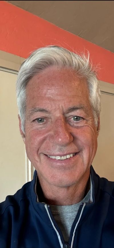 Smiling older man with white hair wearing a navy jacket.