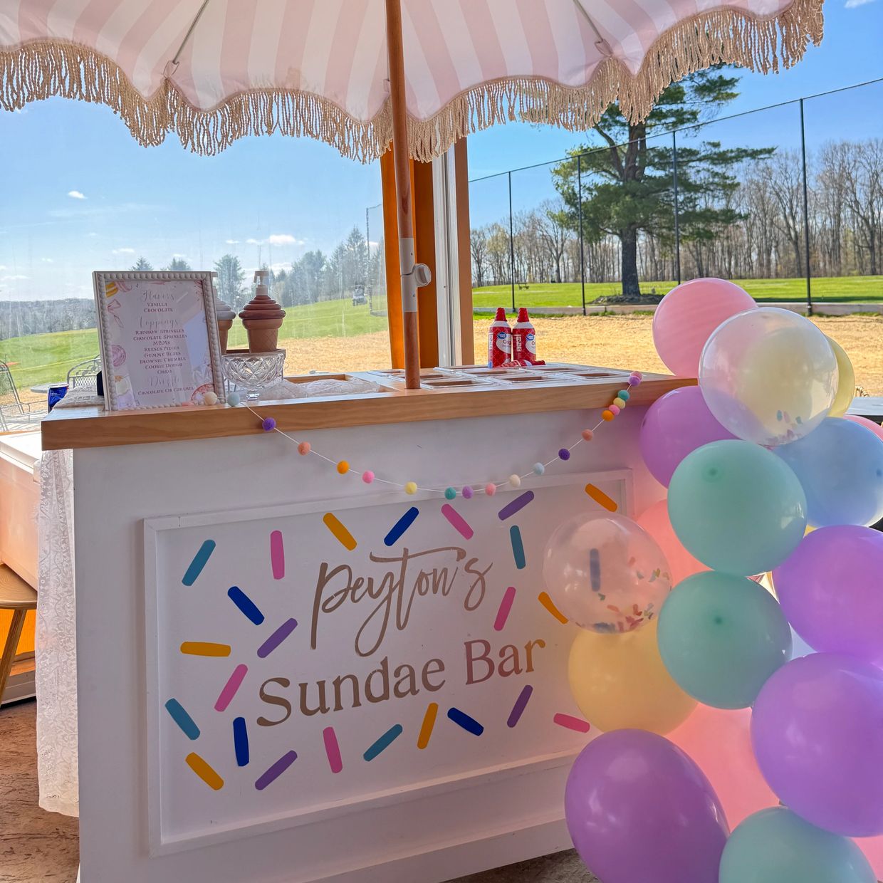 Colorful sundae bar with balloons under a pink umbrella.
