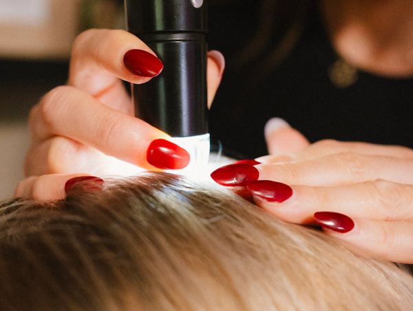 Person with red nails examining scalp with light.