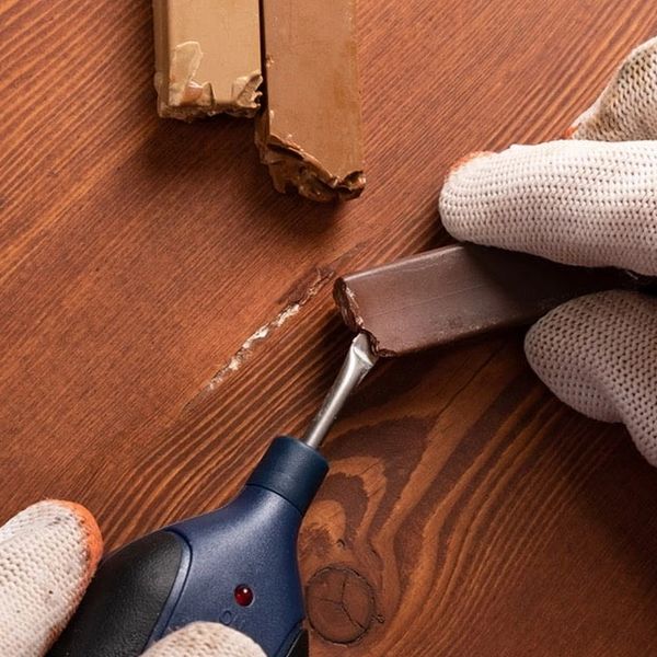 A gloved hand uses a tool to repair a wooden surface with chocolate sticks.