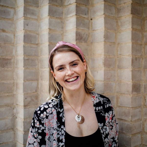 Vicki is wearing a pink headband and black floral top, smiling in front of a neutral background