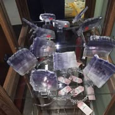 Set of purple-tinted crystal glassware displayed on a glass shelf.