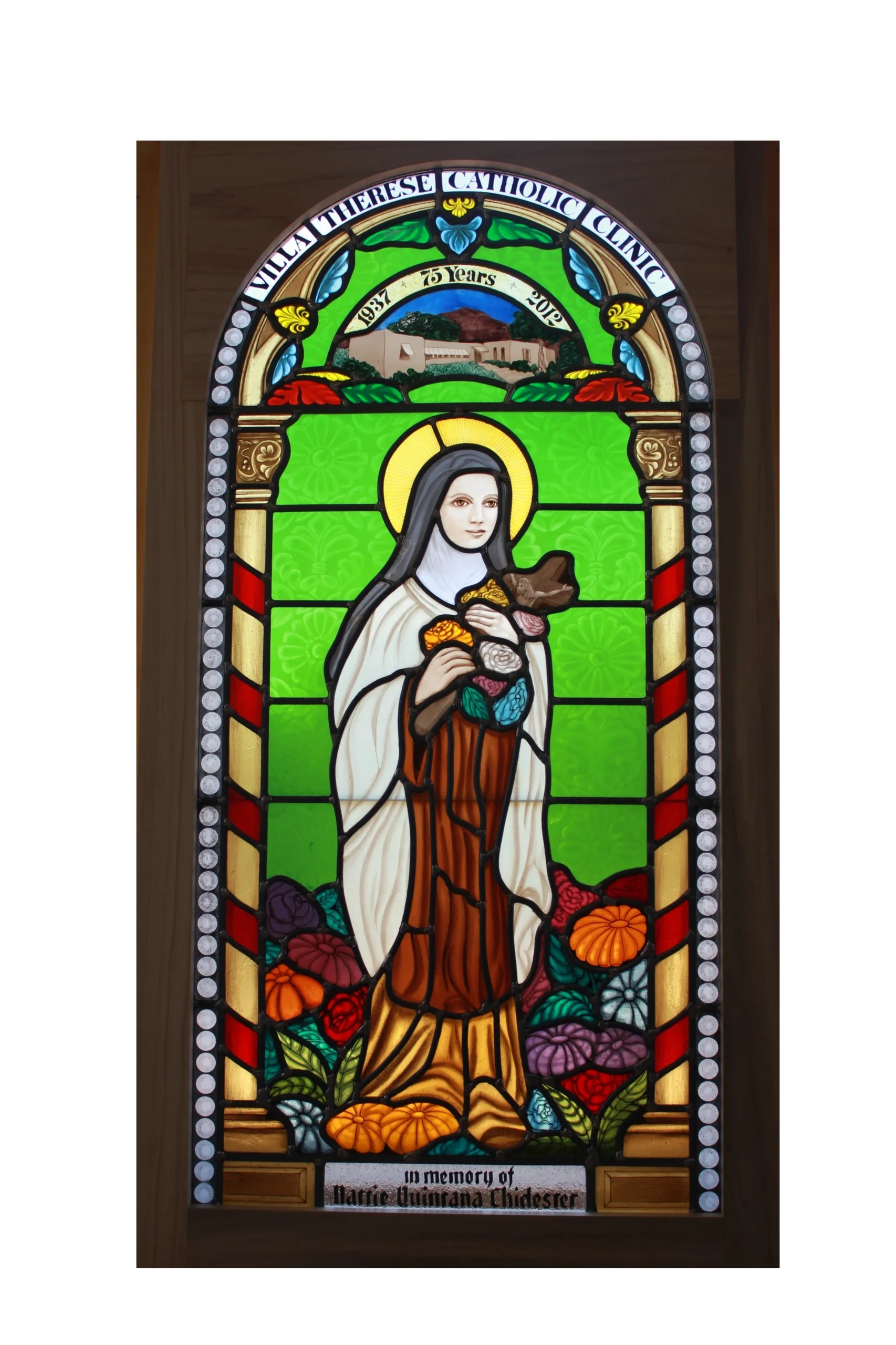 Stained glass window of St Therese holding flowers standing in a bed of colorful flowers