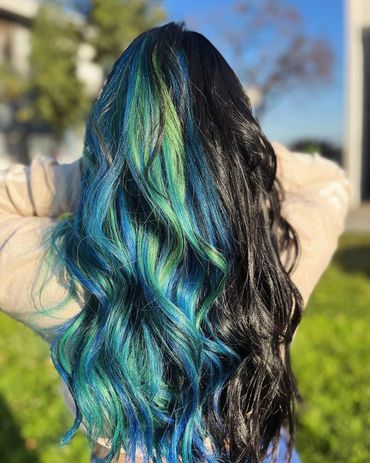 Long wavy hair dyed black with vibrant blue and green highlights outdoors.