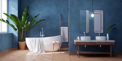 A modern blue painted bathroom, with two vanity sinks, a large white spa tub and light wood flooring