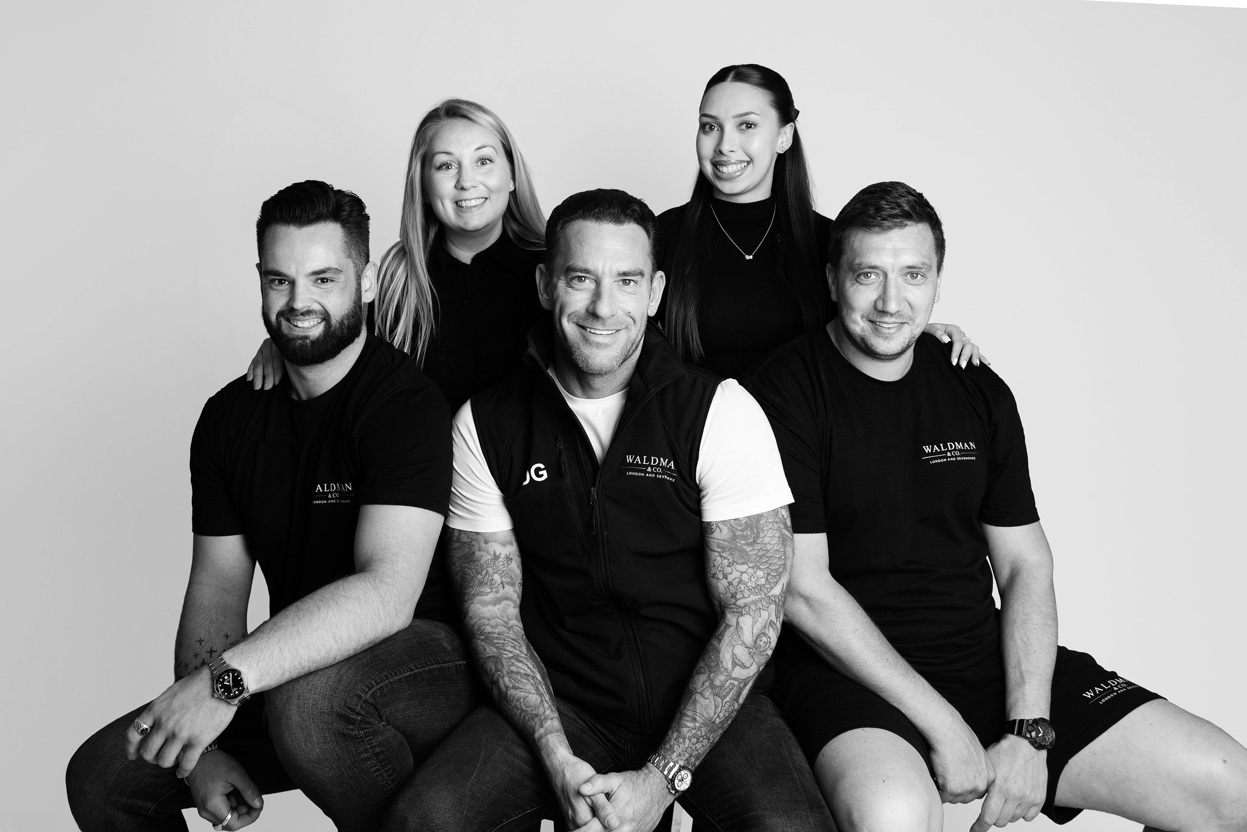 Five smiling people posing together in matching Waldman & Co. attire.